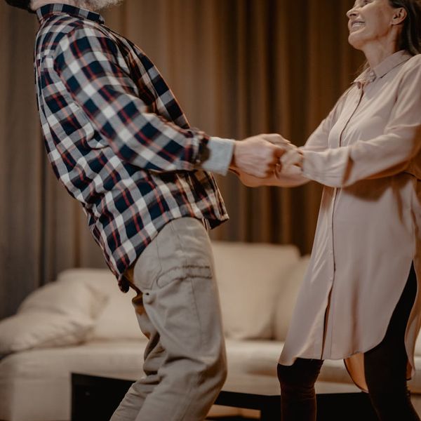 Person of middle age smiling while doing a simple stretching exercise indoors.
